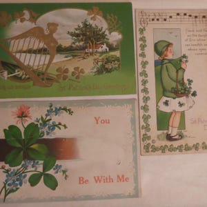 Può includere: Tre cartoline vintage a tema San Patrizio. La prima cartolina presenta uno sfondo verde con un'arpa dorata e trifogli. La seconda cartolina presenta una ragazza con un vestito verde che tiene un cestino di trifogli. La terza cartolina presenta un trifoglio con il testo "You Be With Me".