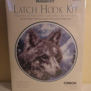 May include: A WonderArt latch hook kit featuring a snow wolf design. The kit includes the materials for a round, 18-inch (45.6 cm) tapestry. The packaging includes text in English, French, and Spanish.