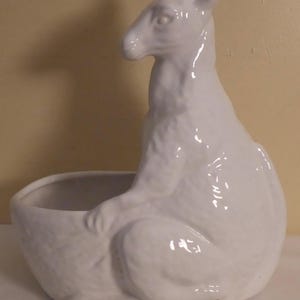 May include: White ceramic planter shaped like a kangaroo. The planter has a smooth, glossy finish and a rounded, bowl-shaped base.