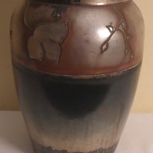 May include: A brown and black ceramic vase with a silver metallic glaze. The vase has a design of leaves and vines on the top half.