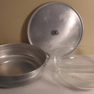 May include: A set of three vintage aluminium serving dishes. The largest dish has a lid with a decorative design. The smaller dish is divided into two sections.