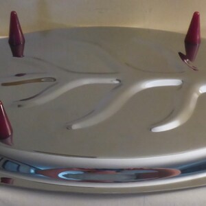 May include: A silver serving tray with a raised, tree-branch design and four red plastic handles. The tray has a raised edge around the perimeter.