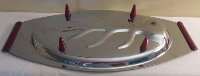 May include: A silver serving tray with a raised, tree-branch design and four red plastic handles. The tray has a raised edge around the perimeter.