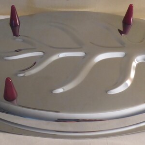 May include: A silver serving tray with a raised tree branch design and four burgundy coloured plastic handles. The tray is oval shaped and has a raised edge.