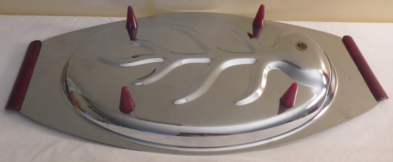 May include: A silver serving tray with a raised tree branch design and four burgundy coloured plastic handles. The tray is oval shaped and has a raised edge.