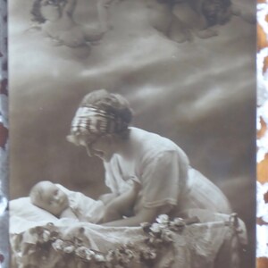 Ancienne carte postale avec photo réelle mère et bébé dans un berceau avec des anges au-dessus, fabriquée en Grande-Bretagne vers le début des années 1900