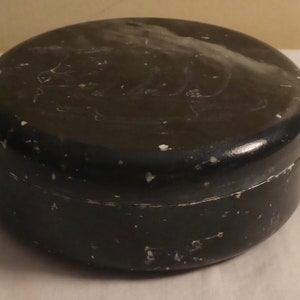 Pu&ograve; includere: Un contenitore rotondo nero con coperchio. Il contenitore ha una finitura leggermente lucida e mostra segni di usura con piccole schegge di vernice bianca. Il coperchio sembra essere leggermente pi&ugrave; chiaro della base.