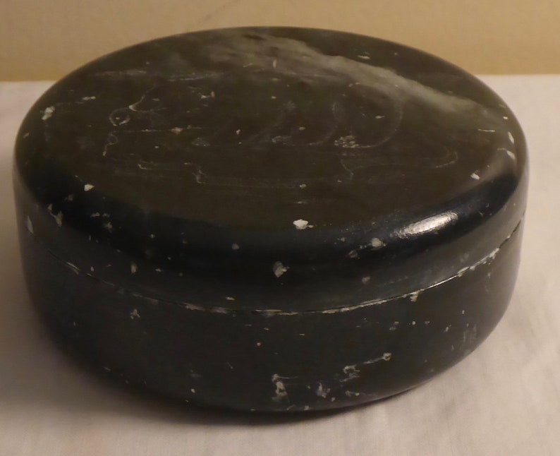 Pu&ograve; includere: Un contenitore rotondo nero con coperchio. Il contenitore ha una finitura leggermente lucida e mostra segni di usura con piccole schegge di vernice bianca. Il coperchio sembra essere leggermente pi&ugrave; chiaro della base.