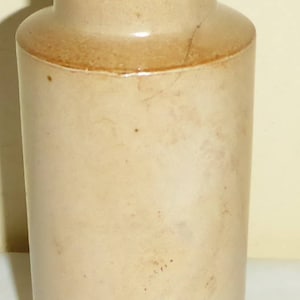 May include: A beige stoneware jar with a wide mouth and a rounded bottom. The jar has a brown glaze and a stamp on the bottom that reads "TRADE MARK REG. NO. 153814".