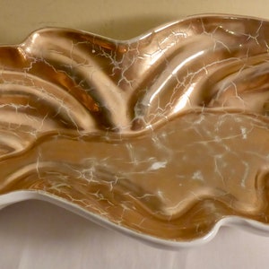 May include: A white ceramic serving dish with a gold metallic glaze. The dish has an organic, free-form shape and a cracked glaze effect.