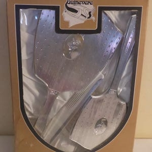 May include: A vintage dressing table set in a box. The set includes a hand mirror, a brush, and a comb, all in a silver-tone finish. The box is brown with the name "Guinevere" and "Dressing Table Set" printed on it.