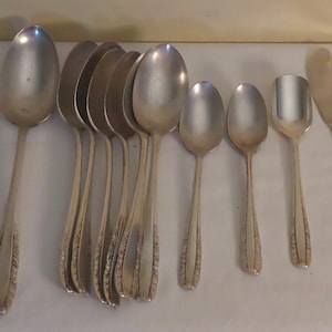 May include: A set of silver cutlery, including forks, spoons, and knives. The cutlery is arranged in a row on a white surface.