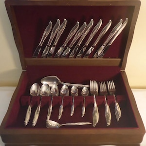 May include: A wooden box with a red velvet interior containing a set of cutlery. The cutlery includes forks, knives, and spoons.
