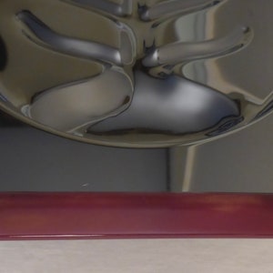 May include: A silver-coloured metal serving tray with a unique design. The tray has a raised, rounded edge and a base made of a dark red material.