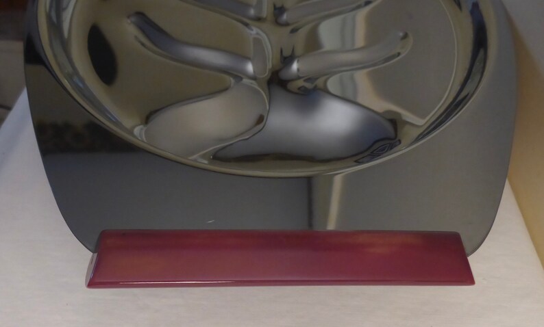 May include: A silver-coloured metal serving tray with a unique design. The tray has a raised, rounded edge and a base made of a dark red material.