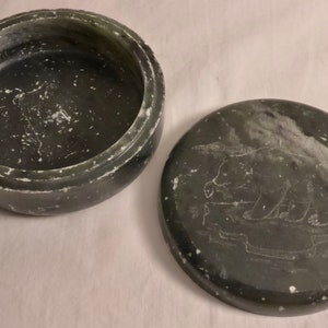 Pu&ograve; includere: Scatola portagioie rotonda verde scuro con coperchio. Il coperchio presenta un disegno di orso inciso. La scatola &egrave; aperta, rivelando l'interno. La scatola e il coperchio hanno un aspetto strutturato con accenti bianchi.