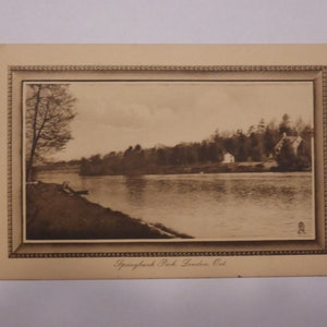 Pode incluir: Um cart&atilde;o postal vintage em preto e branco com uma vista panor&acirc;mica do Springbank Park em London, Ont&aacute;rio. O cart&atilde;o postal mostra um rio com &aacute;rvores que margeiam as margens e uma casa ao longe.