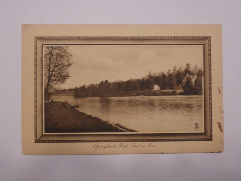 Pode incluir: Um cart&atilde;o postal vintage em preto e branco com uma vista panor&acirc;mica do Springbank Park em London, Ont&aacute;rio. O cart&atilde;o postal mostra um rio com &aacute;rvores que margeiam as margens e uma casa ao longe.