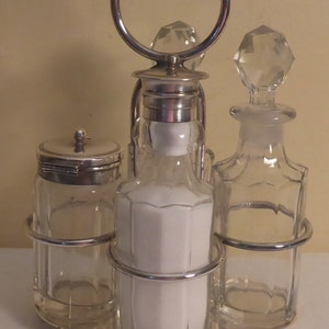 May include: Silver plated condiment set with four glass bottles. The bottles have crystal stoppers and are held in a silver plated stand with a ring handle.