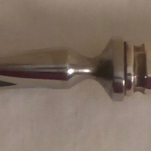 May include: A silver fish serving utensil with a long, curved handle and a pointed end.