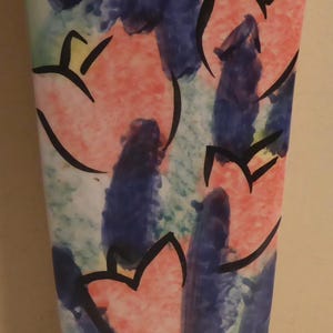 May include: A ceramic vase with a colorful abstract design featuring pink, blue, and green hues. The vase has a tall, rectangular shape and is decorated with stylized flowers.