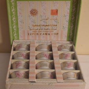 May include: A box of 12 white ceramic teacups with pink floral designs. The box is decorated with a pink and white striped pattern and the text "12PCS CAWA CUP".