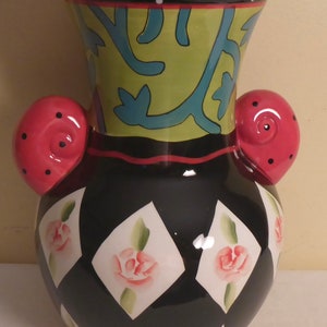 May include: A black and white ceramic vase with pink rose accents and two pink handles. The vase has a diamond pattern and a green floral design around the top.