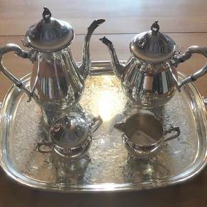 May include: A silver tea set on a silver tray with an ornate design. The set includes a teapot, creamer, and sugar bowl.