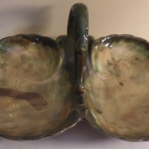 May include: A green and brown ceramic serving dish with two sections and a handle. The dish is shaped like a pair of clamshells.