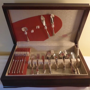 May include: A wooden box with a red velvet lining and a set of 1847 Rogers Bros. silverware. The silverware is arranged in the box, with the knives, forks, and spoons separated into different compartments. The box is closed, and the lid is open.