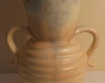 May include: A ceramic vase with two handles, featuring a light blue and yellow glaze with a textured, ribbed design.