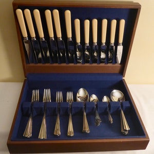 May include: A wooden box with a blue velvet lining containing a set of silver cutlery. The cutlery includes knives, forks, and spoons. The handles of the knives are made of ivory.
