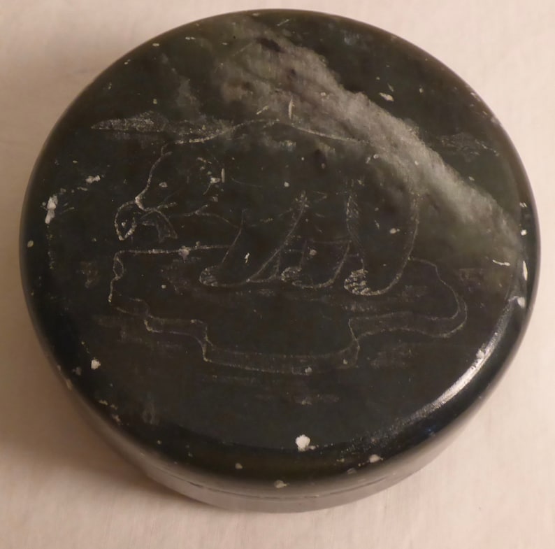 Pu&ograve; includere: Intaglio in pietra rotonda verde scuro con un orso inciso su una superficie rialzata. L'orso &egrave; in piedi su un piccolo iceberg. La pietra presenta macchie bianche e una finitura lucida.