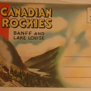 May include: A vintage postcard featuring a scenic view of the Canadian Rockies with a train traveling through a mountain pass. The postcard has the text "CANADIAN ROCKIES BANFF AND LAKE LOUISE" and a small Canadian flag in the top left corner.