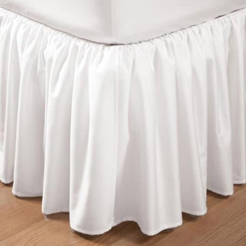 May include: White bed skirt with a ruffled edge. The skirt is made of a soft, smooth fabric and is designed to cover the box spring of a bed.