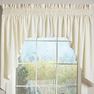 May include: Cream-colored window valance with a gathered top and a scalloped bottom edge. The valance hangs over a window with a view of a blurred outdoor scene. The fabric is a solid, neutral color, suitable for various interior styles.