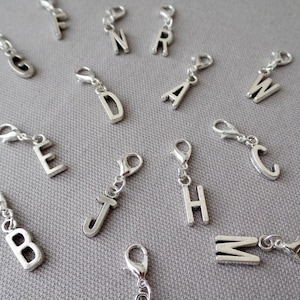 May include: A set of silver letter charms with a lobster clasp. The letters include A, B, C, D, E, F, G, H, J, K, M, N, R, V, W, and Z.