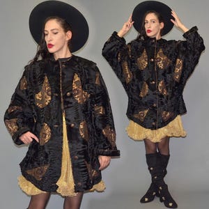 Puede incluir: Abrigo negro con detalles decorativos dorados. El abrigo tiene un aspecto texturizado y está abotonado. La modelo lleva una falda dorada y un sombrero negro. Es un artículo de moda vintage.