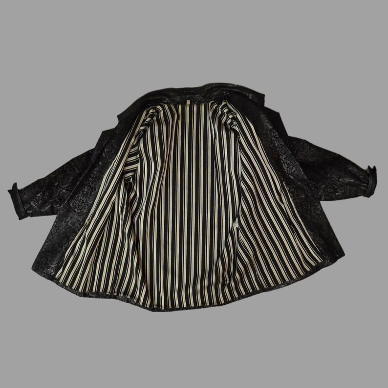 May include: A black jacket with a textured, embossed floral pattern on the exterior and a contrasting interior lining featuring vertical black and white stripes. The jacket has long sleeves with cuffs and is displayed in an open, flat position.