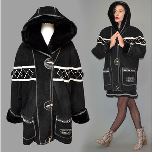 May include: A black hooded coat featuring a white geometric pattern across the chest and sleeves, two large front pockets, and toggle closures. The hood and cuffs are trimmed with black faux fur, and the coat has white stitching details.