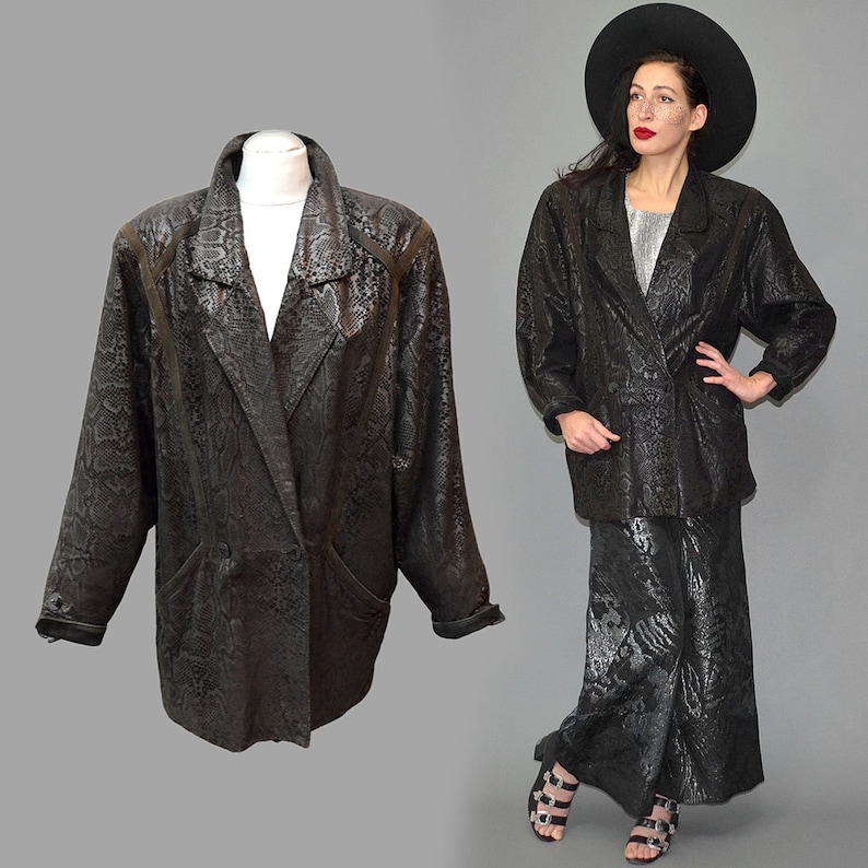 May include: A black blazer featuring a subtle snakeskin texture pattern, a notched lapel, and a double-breasted front closure. The garment has long sleeves with cuffs and structured shoulders, presented on a mannequin and worn with a matching skirt.