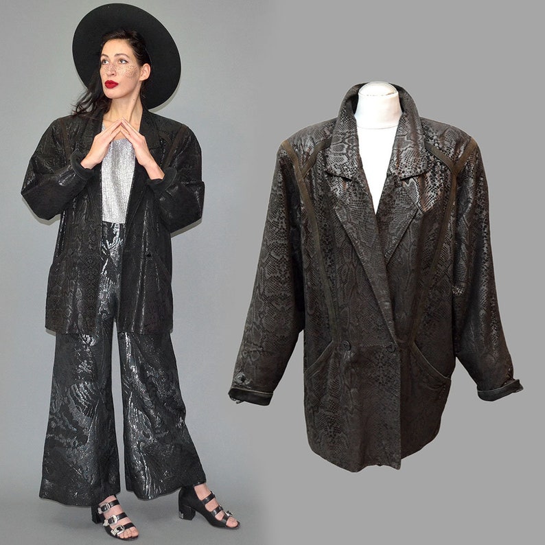 May include: A black blazer featuring a textured snakeskin pattern, a notched lapel, long sleeves, and a double-breasted front closure with buttons. The jacket is displayed on a mannequin, showcasing its structured shoulders and tailored fit.