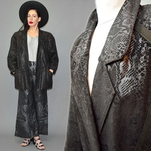 Puede incluir: Un conjunto de blazer negro y pantalones anchos a juego con un patrón de piel de serpiente tonal. La chaqueta tiene solapa de muesca, mangas largas y dos bolsillos delanteros. Los pantalones son de talle alto y corte holgado.