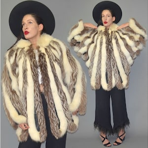 May include: A vintage fur coat featuring cream and brown vertical stripes. The coat has a wide collar and a voluminous shape. The model is wearing a black hat and black trousers. The coat appears to be in excellent condition.
