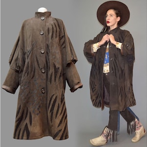 Può includere: Un cappotto in camoscio marrone con collo alto e chiusura con bottoni. Il cappotto presenta un motivo unico di forme astratte marrone scuro. L'immagine mostra anche una persona che indossa il cappotto, abbinato a jeans e stivali e un cappello a tesa larga.