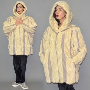 May include: Cream-colored hooded coat with vertical gray stripes. The coat has a chevron pattern and a zip-up front. The model is wearing black velvet pants and sparkly sneakers. The coat is a vintage style.