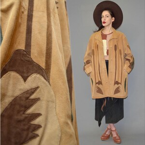 May include: A tan suede jacket featuring long sleeves, a button-front closure, and a collar. The jacket is decorated with dark brown suede appliqué patterns of tall, slender plant-like shapes and leaf motifs along the front and sleeves.