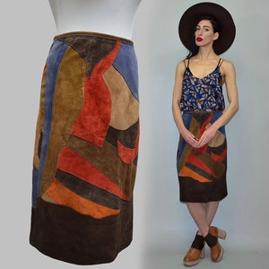 Op de afbeelding: Een vintage suède rok met een patchwork ontwerp in bruin, oranje, blauw en tan. De rok heeft een potloodsilhouet en een donkerbruine zoom. De rok wordt getoond op een mannequin en een persoon.