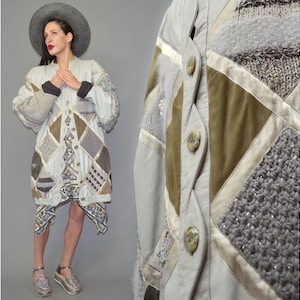 May include: A long-sleeved jacket featuring a patchwork design of light gray, olive green, and cream panels. The garment incorporates various textures including knit, satin, and smooth fabric, finished with a front button closure and round buttons.