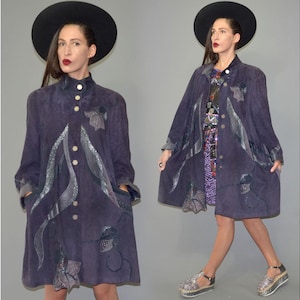 May include: A vintage, dark purple suede coat with decorative silver accents and button closures. The coat features a long, flowing design with a high collar and pockets. The model is wearing a black hat and platform sandals. A unique, retro fashion statement.